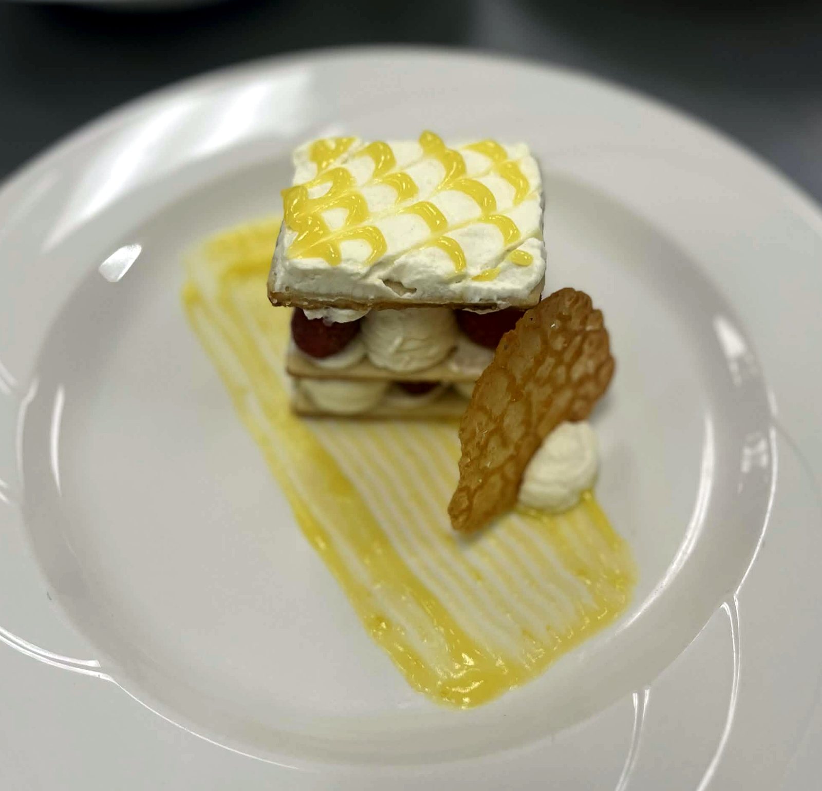 A layered napoleon pastry with a lattice top and a thin tuile on a white plate