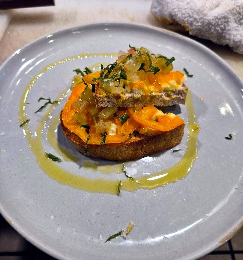 Tomato toast with stracciatella, yellow tomato and basil on a grey plate