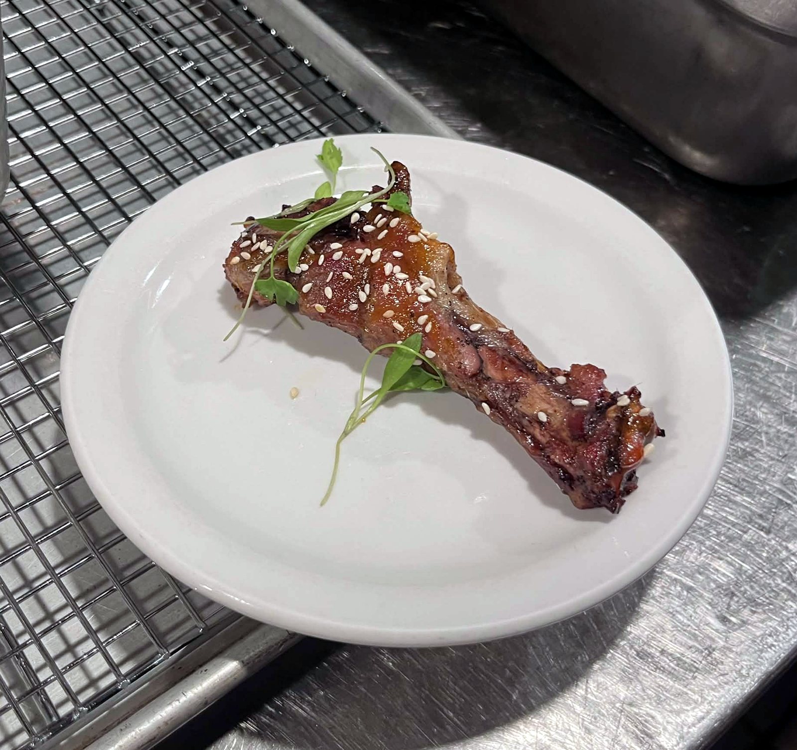 A glazed duck drumette with sesame seeds and cilantro on a small white plate