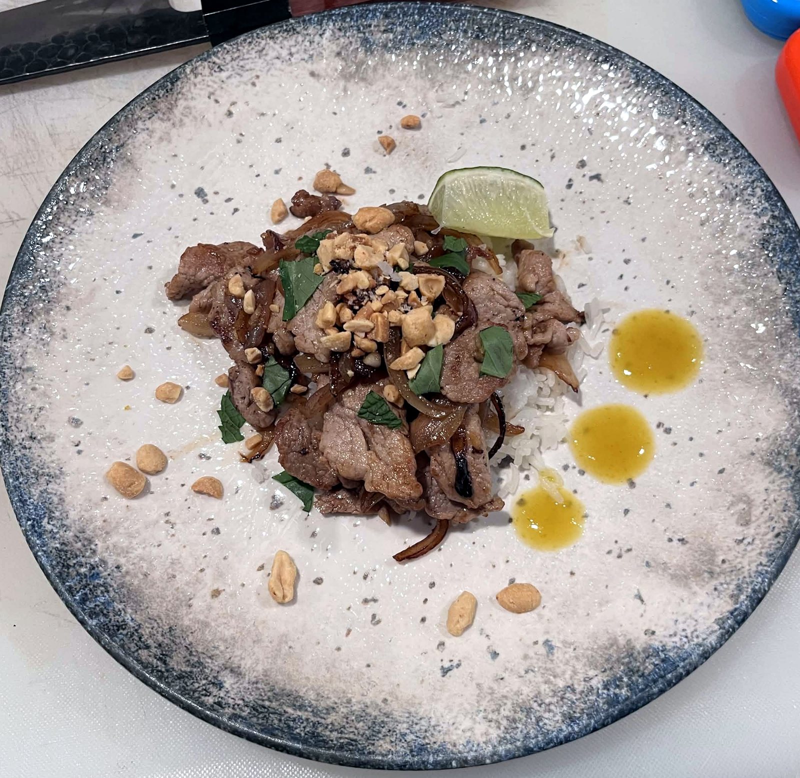 Sliced pork with peanuts, herbs and lime on a blue speckled plate