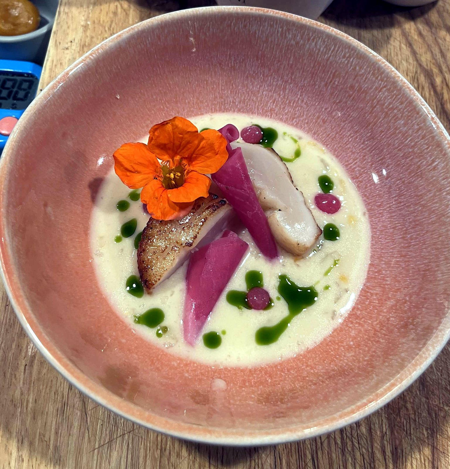 Seared scallop in creamed corn with basil oil and a nasturtium flower in a pink bowl
