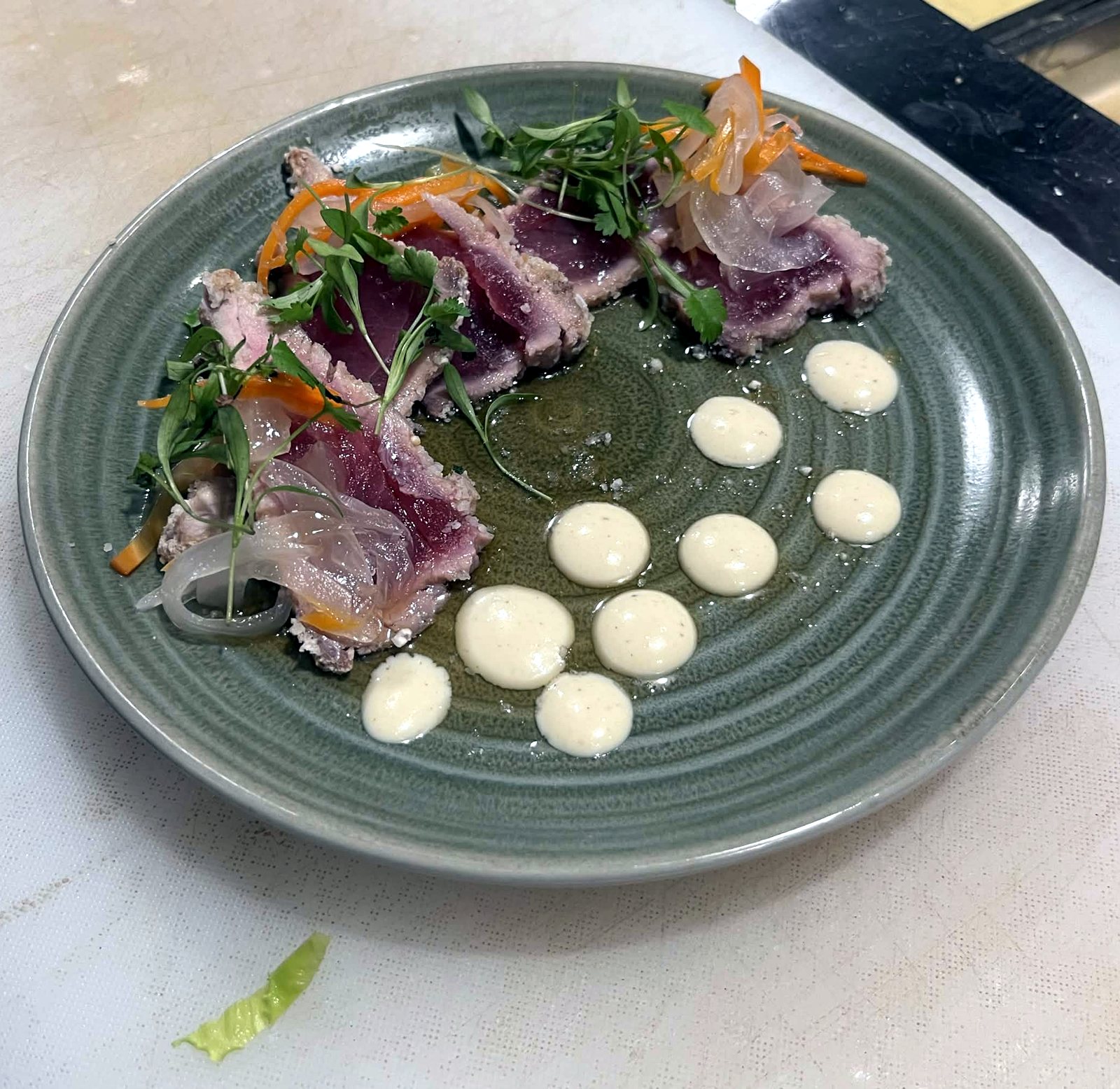 Sliced seared tuna with dots of aioli and microgreens on a green plate